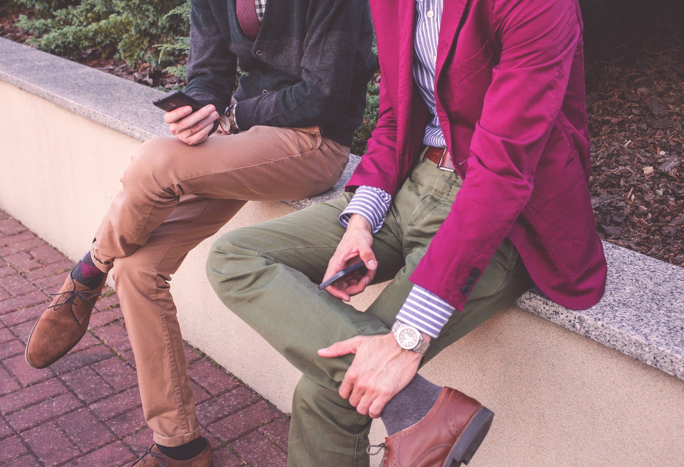 Dois homens sentados, um de blazer pink e calça de sarja, outro de calça cáqui