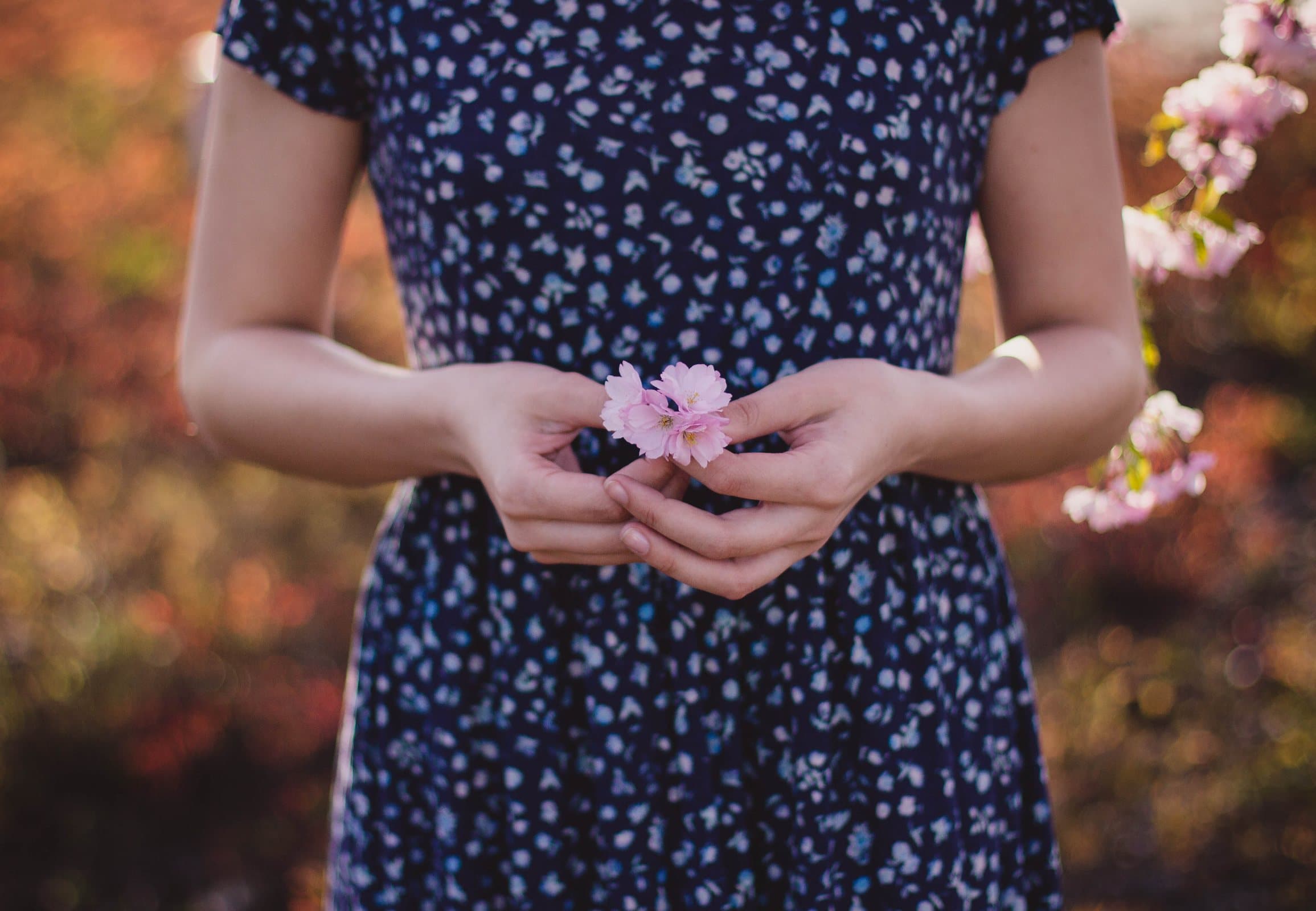 Mulher com vestido midi azul de estampa miúda segurando uma pequena flor rosa