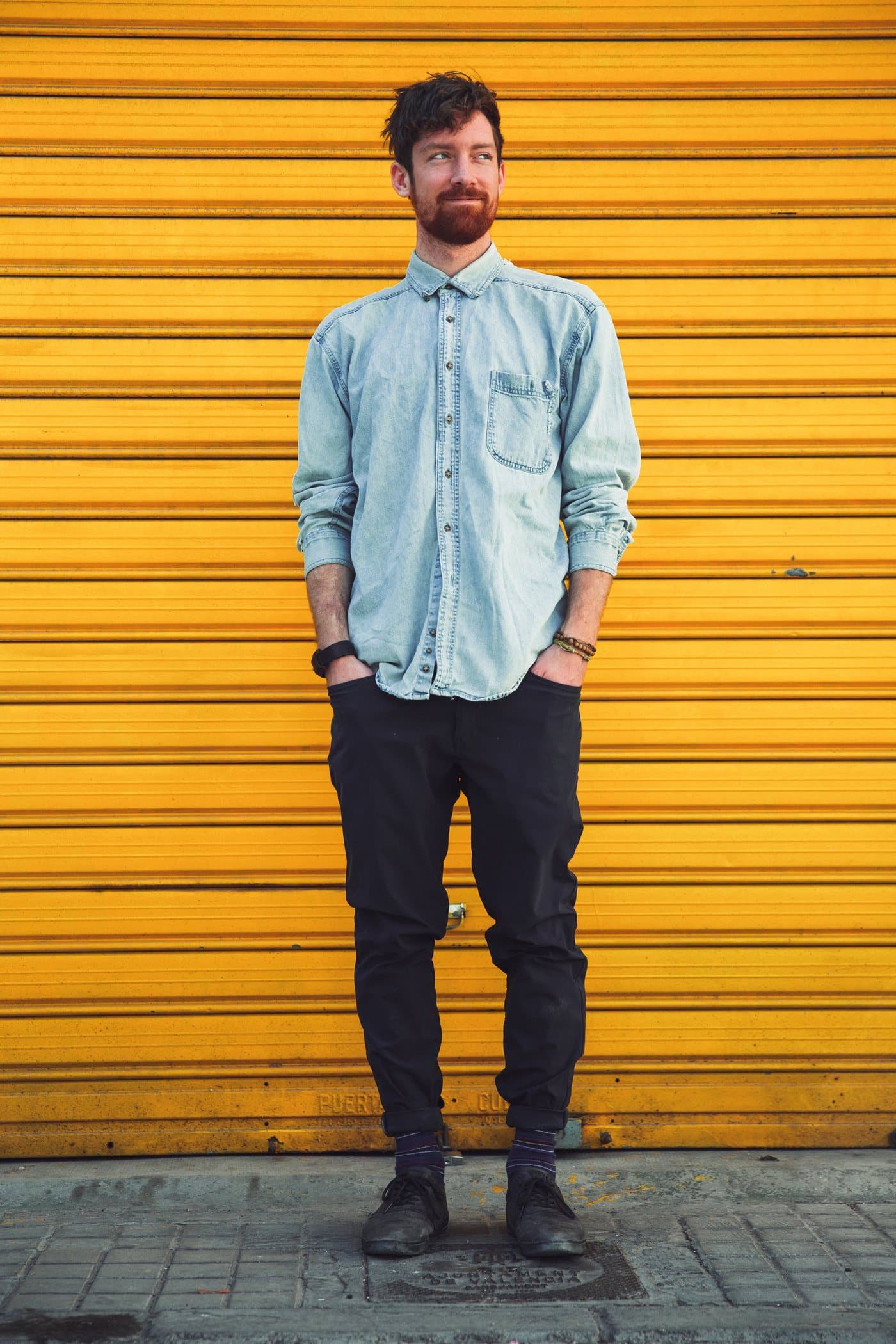 Homem de camisa jeans clara com mangas dobradas e calça escura